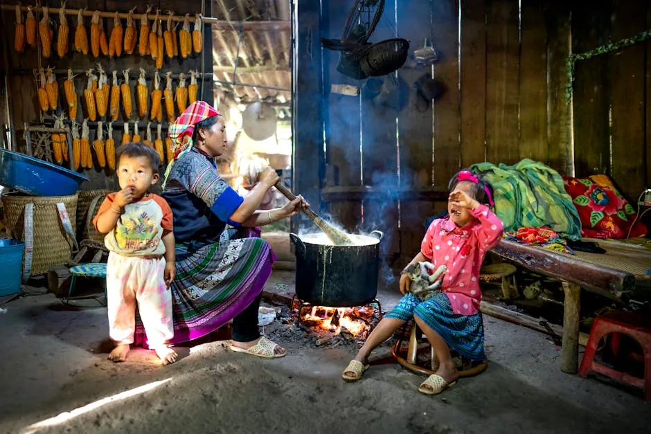 Side view of Asian woman in colorful outfit sitting with children and preparing food on bonfire in wooden rural barn in daytime