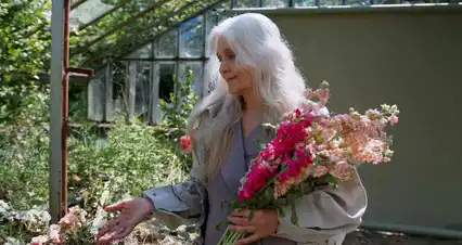 Horizontal video: Woman looking at flowers in front of greenhouse 10049403. Duration: 64 seconds. Resolution: 4096x2160