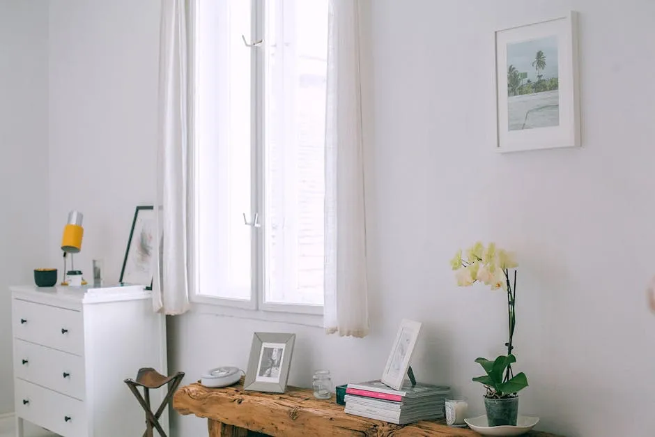 Interior of cozy room with photo frames and flowerpot placed on wooden counter near white wall with picture and window