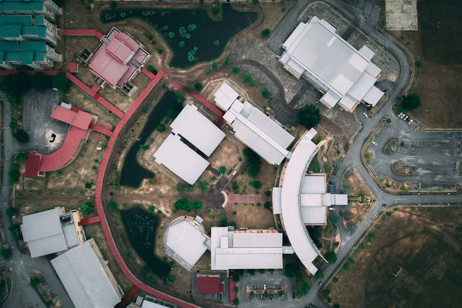 Top view of different constructions with white and red roofs surrounded by roads and long fences near ponds with green plants in daytime