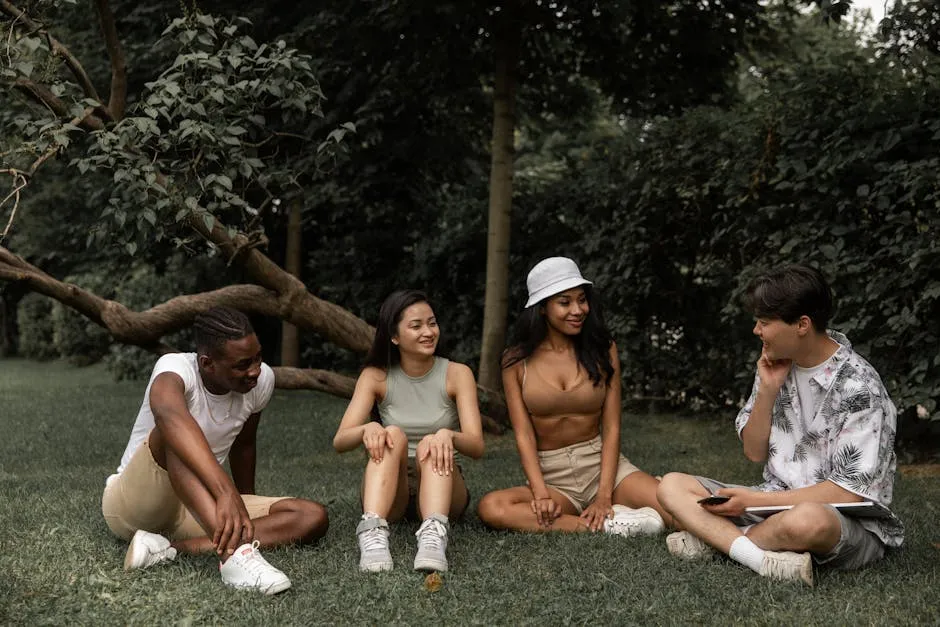 Group of multiracial friends relaxing on grass in park while speaking and looking at each other