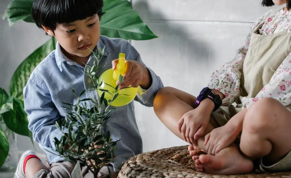 Crop Asian child in casual clothes spraying fresh water on plant while sitting with sister at home