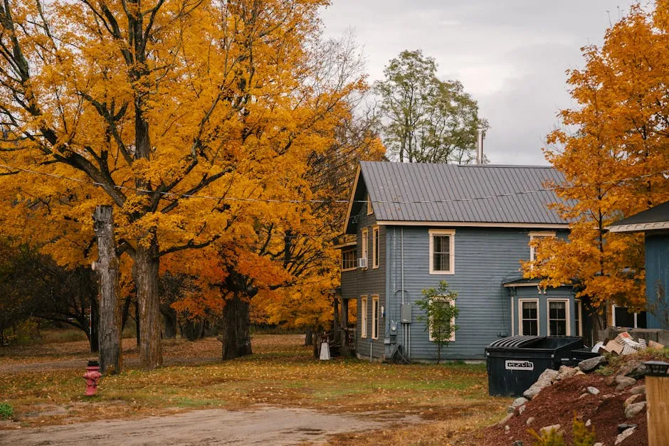 Cottage with triangular roof surrounded by tall trees with vibrant yellow leaves in autumn